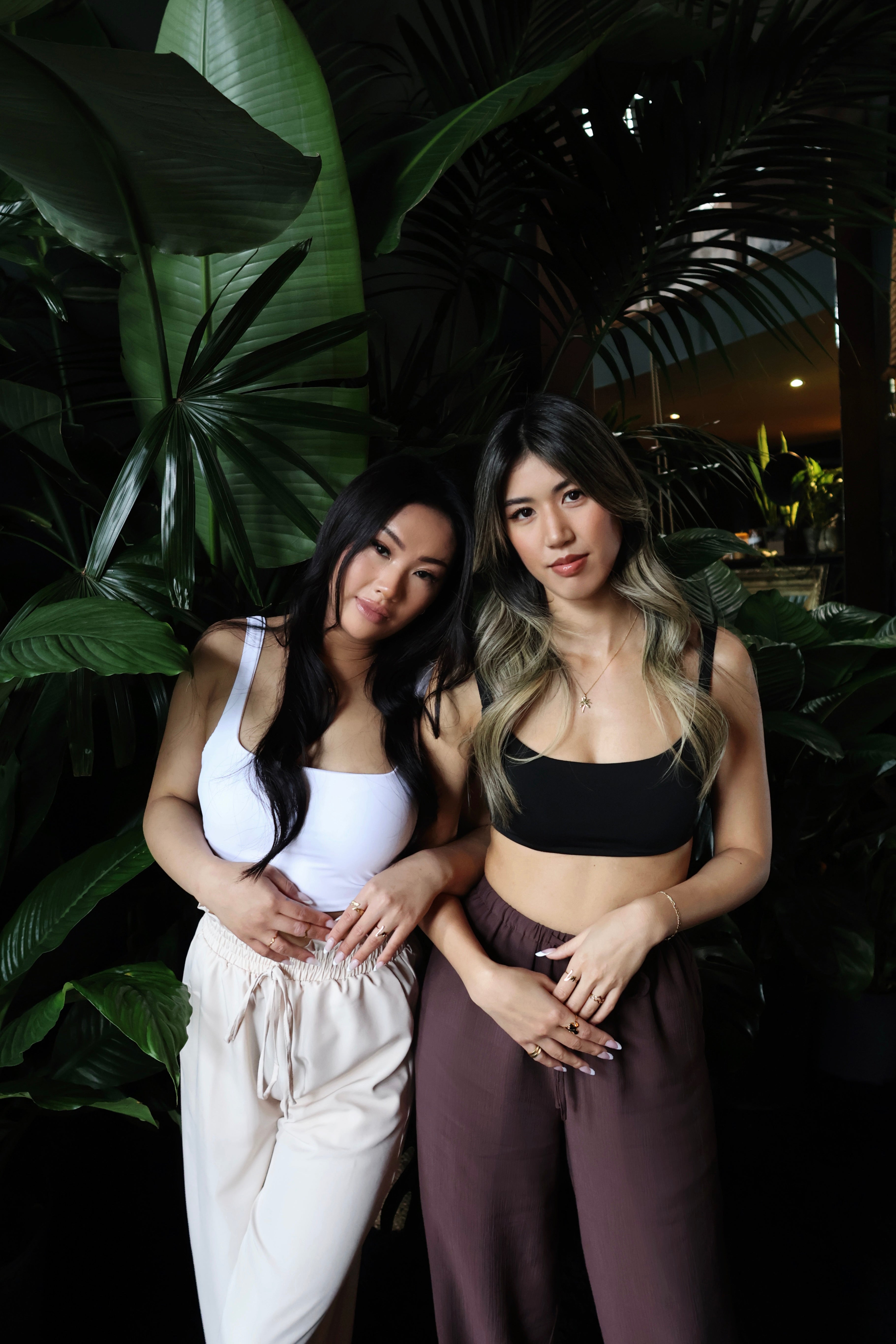 two women modeling gold rings, bracelets necklaces tropical leafy background